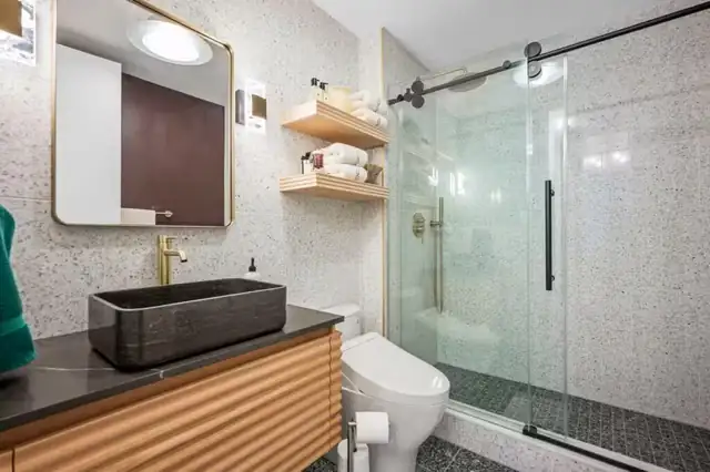 Bathroom remodel with fluted wood vanity, black stone vessel sink, terrazzo-look tile and sliding glass shower door