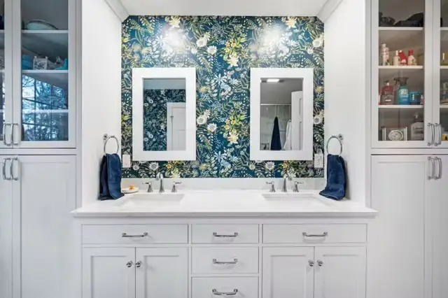 Double vanity bath remodel with botanical wallpaper, white framed mirrors and built-in linen towers