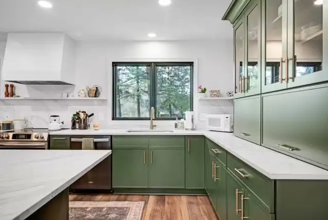 Kitchen remodel with sage green shaker cabinets, glass-front uppers, white range hood and marble-look counters