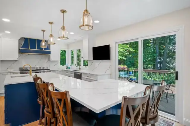 Kitchen remodel with navy blue island, white quartz top, brass pendant lights and wood chairs by a sliding door