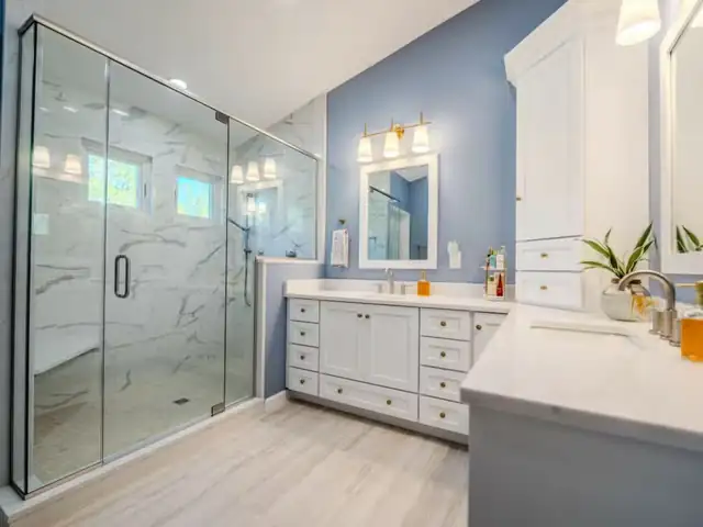 Bathroom remodel with frameless glass walk-in shower, marble-look wall tile, blue accent wall and white vanity